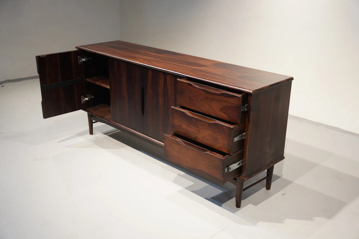 A mid-century modern wooden sideboard with a rich dark brown finish, featuring an open cabinet door on the left, three drawers on the right, and open shelving in the center, photographed in a minimalist studio setting.