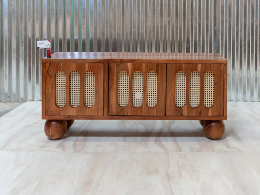 A mid-century modern wooden sideboard cabinet with three doors featuring woven cane panels, shown on a light wood floor against a corrugated metal wall.