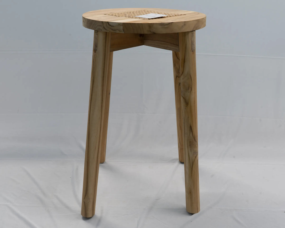 A light natural wood stool with a round woven cane seat and three tapered legs, photographed against a white fabric backdrop.