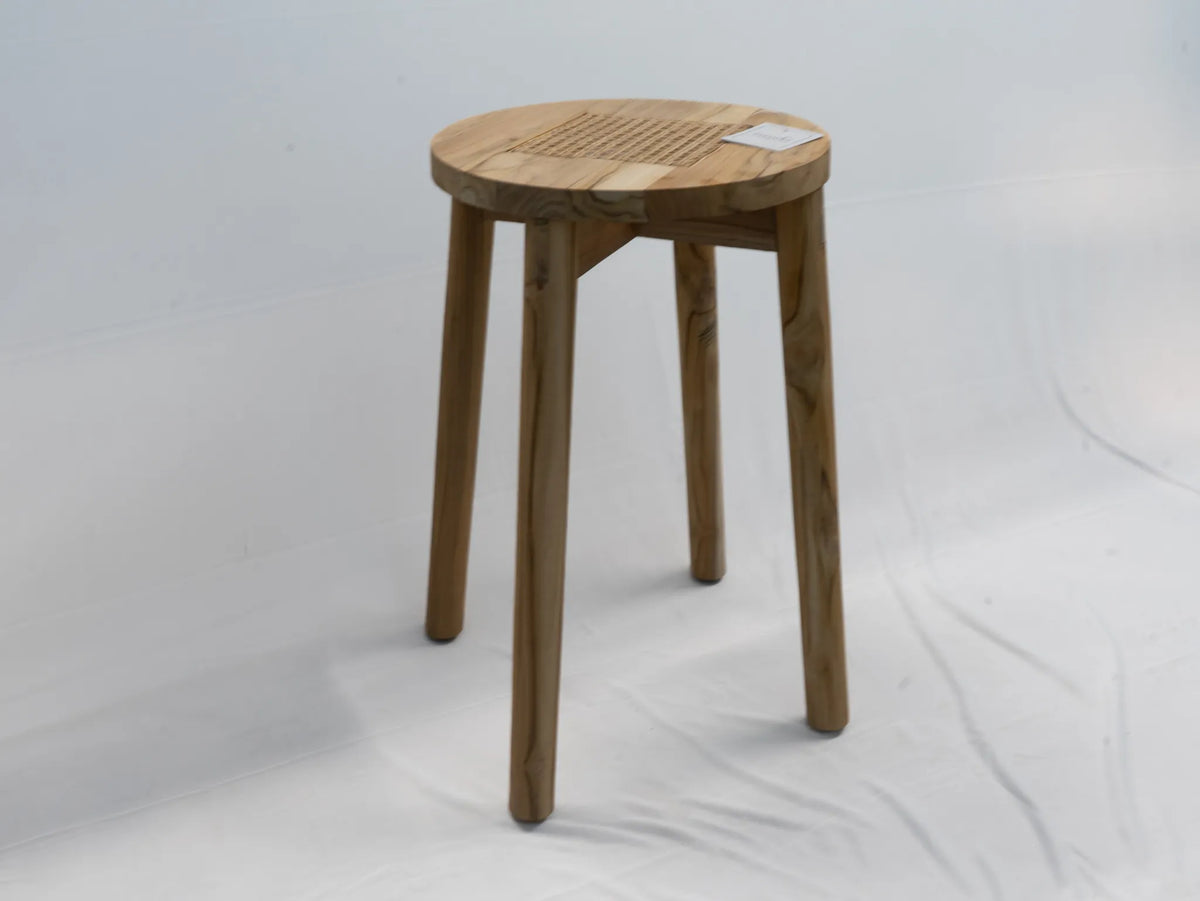 A round teak wooden stool with four legs and rattan cane detail, shown on a white studio background.