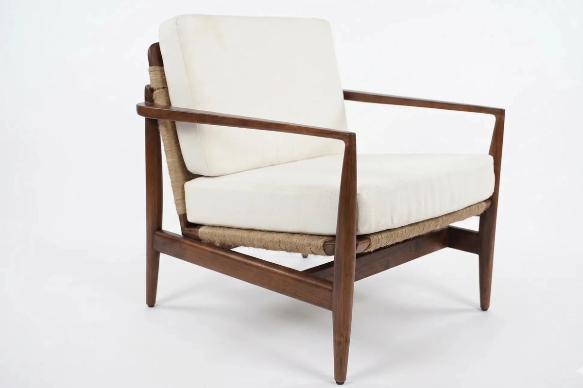 A mid-century modern accent chair featuring a dark brown wooden frame, woven natural fiber armrests and seat, and off-white cushions, shown against a plain white background.