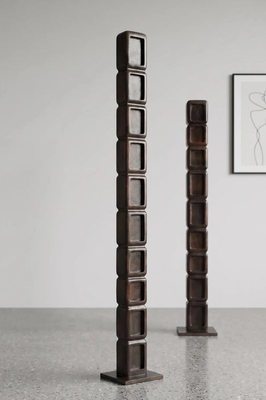 Two tall dark brown wooden decorative wooden sculpture units with square recessed panels, standing on a speckled gray floor against a light gray wall to decor your space