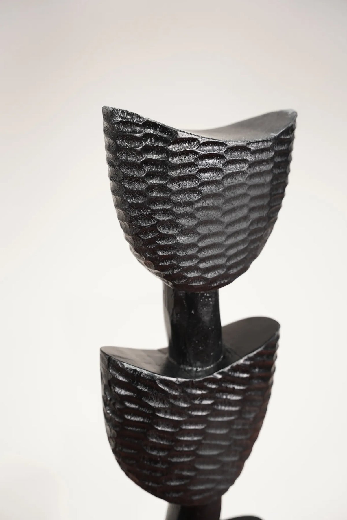 A modern black sculptural floor decor featuring two textured, bowl-like tiers on a slim central stem, photographed against a neutral light gray background.