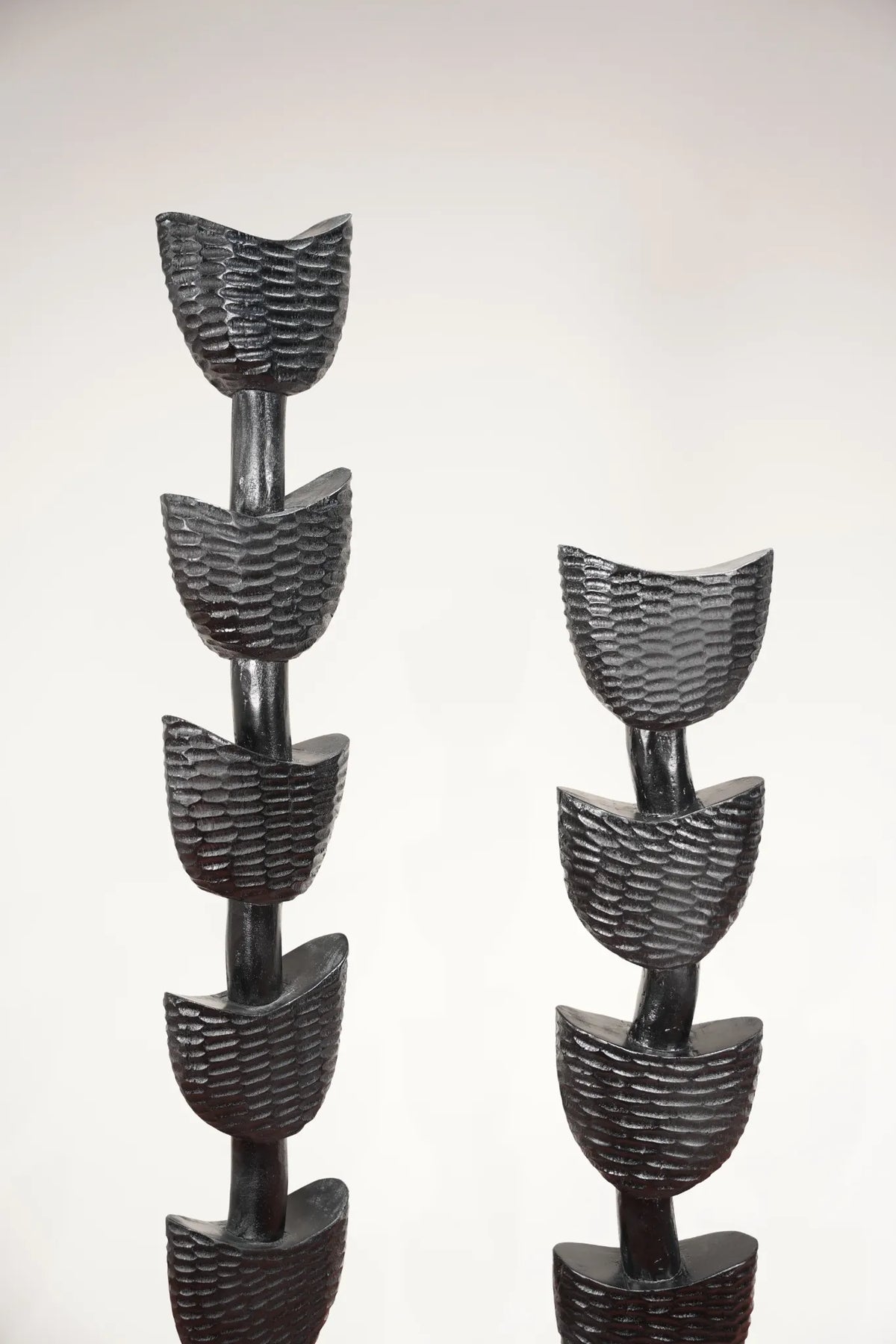 Two black textured decorative sculptures with stacked leaf-like or petal-like segments on a plain light background.