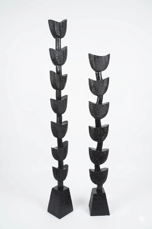 Two black abstract decorative sculptures with stacked leaf-like or petal-like forms on tapered rectangular bases, photographed against a plain light gray studio background.