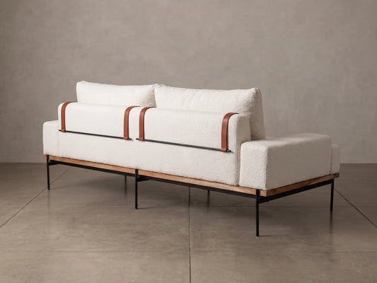 A modern white bouclé sofa with brown leather accents and a black metal frame, set against a neutral gray concrete wall and floor.