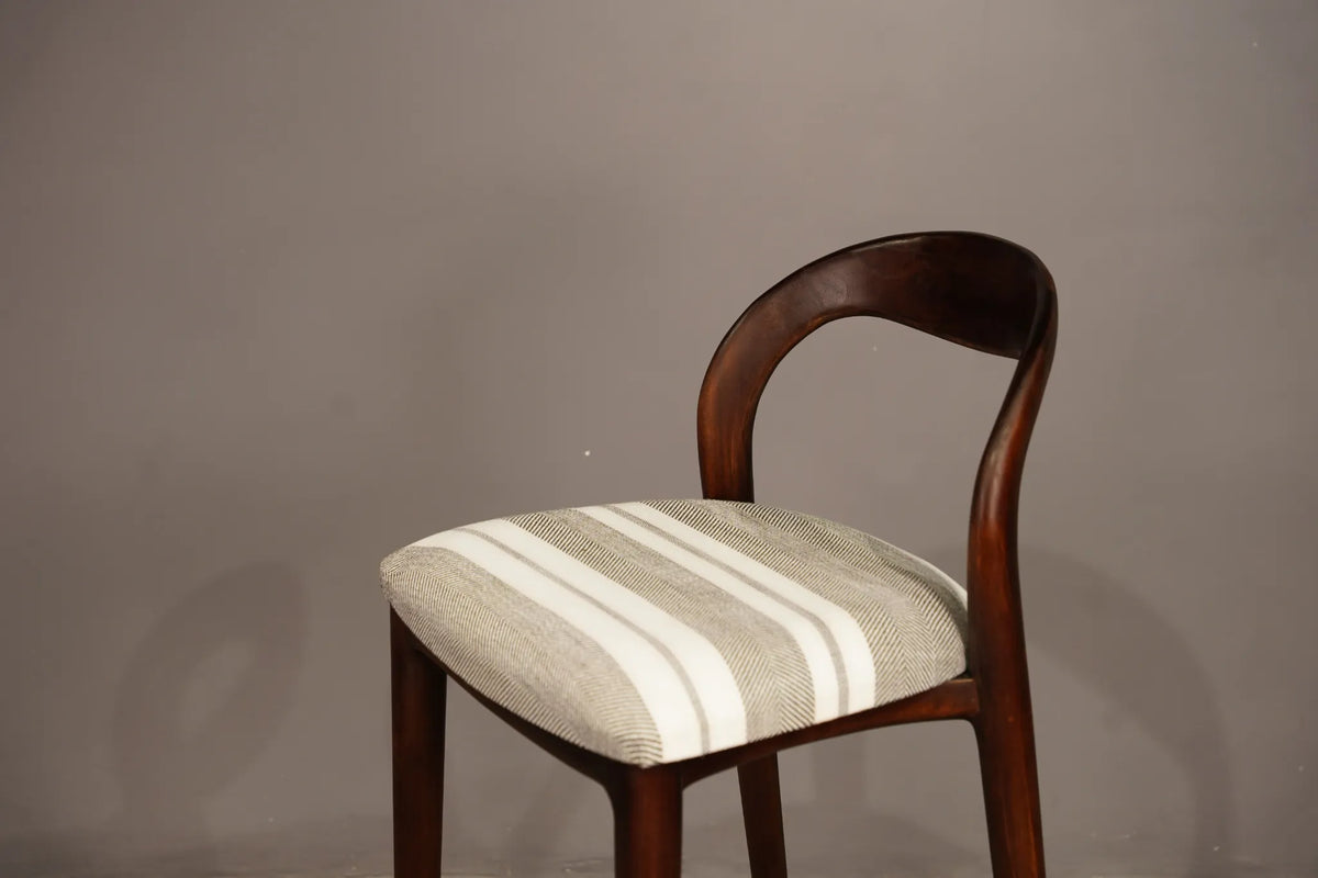 A wooden dining chair with a curved backrest and a striped upholstered seat cushion in beige and white, set against a plain gray wall.
