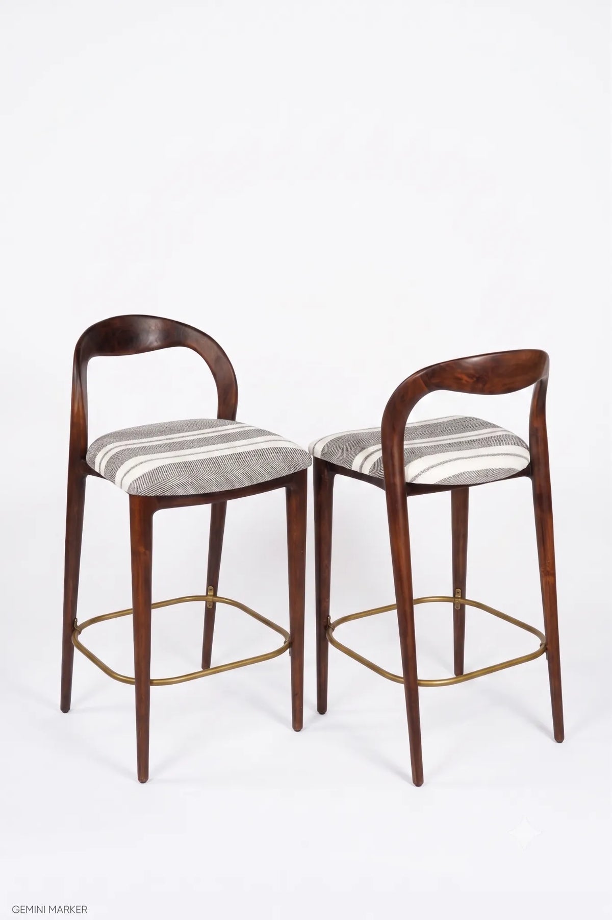 Two modern bar stools with curved dark wood backs and seats upholstered in a gray and white striped fabric, featuring brass-colored metal legs and footrests, shown against a plain white background.