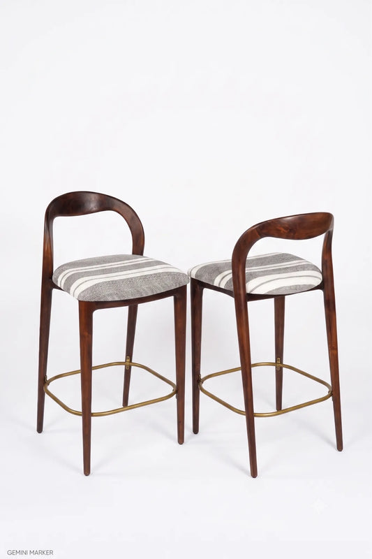 Two modern bar stools with curved dark wood backs and seats upholstered in a gray and white striped fabric, featuring brass-colored metal legs and footrests, shown against a plain white background.