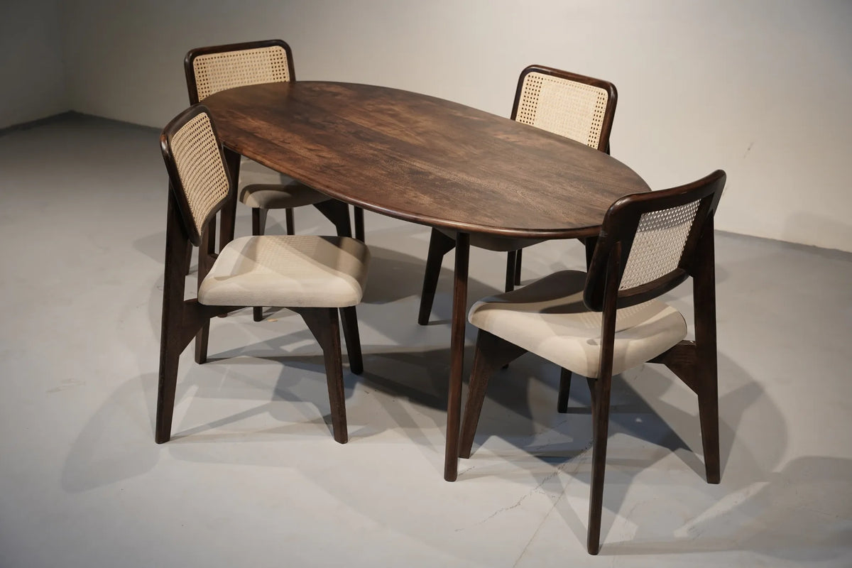 An oval wooden dining table with four matching chairs featuring dark wood frames and woven cane backs, set against a neutral gray studio background.
