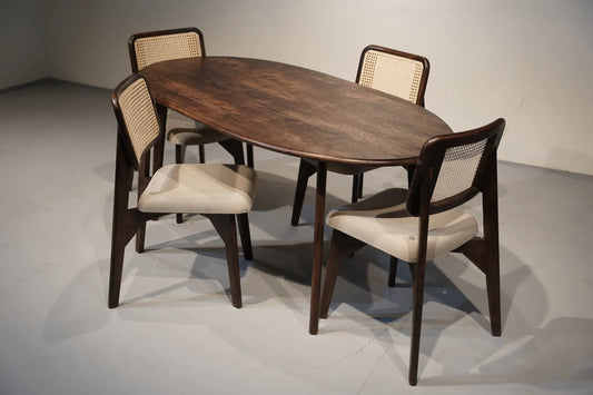 An oval wooden dining table with four matching chairs featuring dark wood frames and woven cane backs, set against a neutral gray studio background.