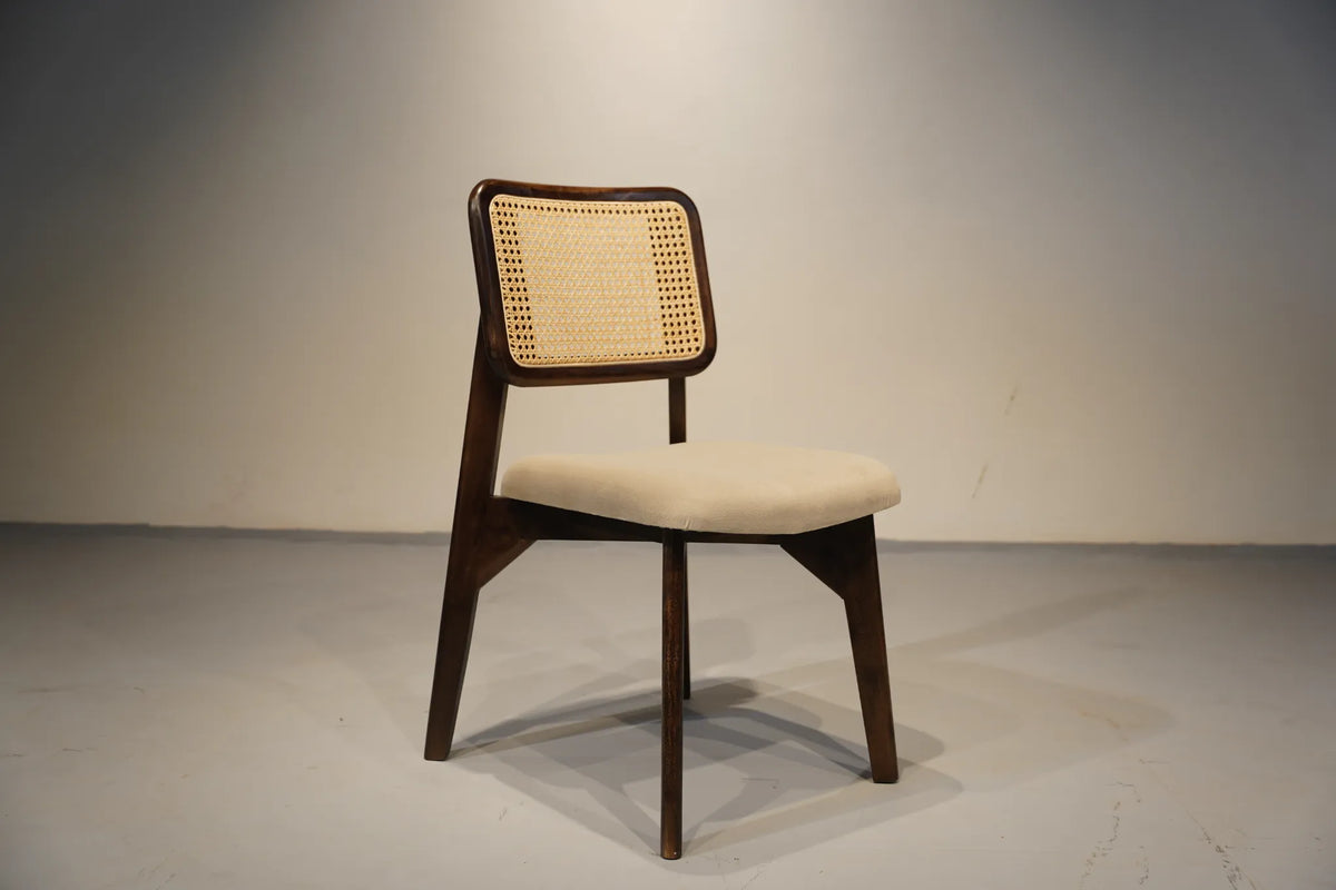 A mid-century modern dining chair with a dark wood frame, a woven cane backrest, and a light beige upholstered seat, shown against a neutral gray studio background.