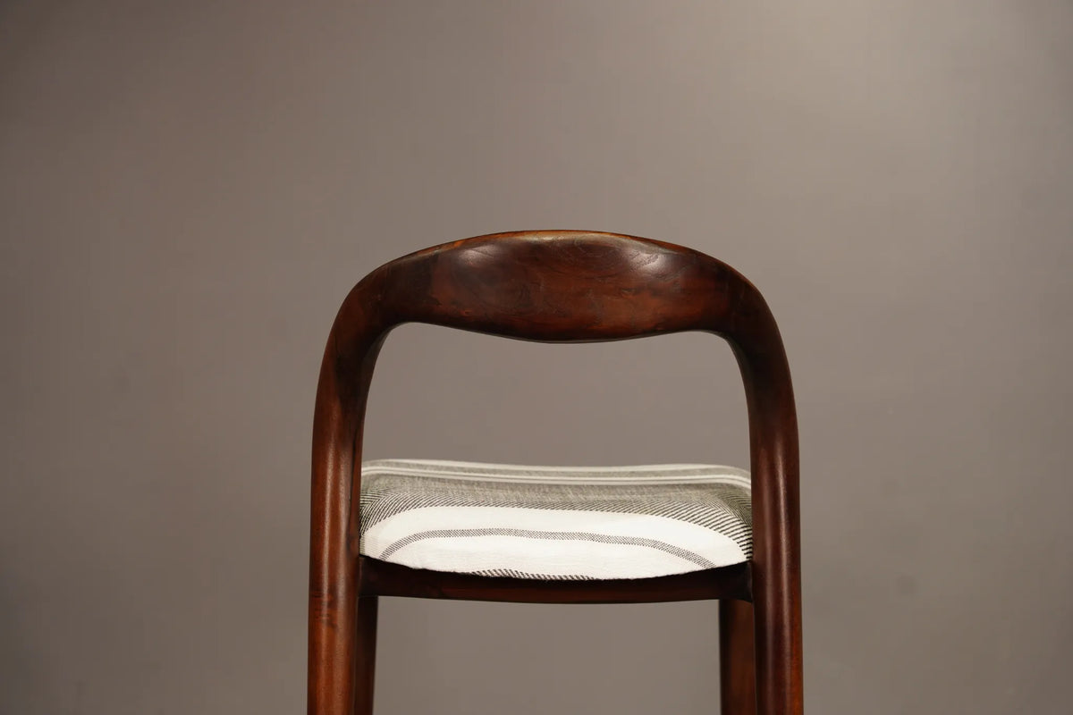 A close-up of a wooden chair back with a curved, polished dark brown wood finish and a striped fabric cushion in white and gray.