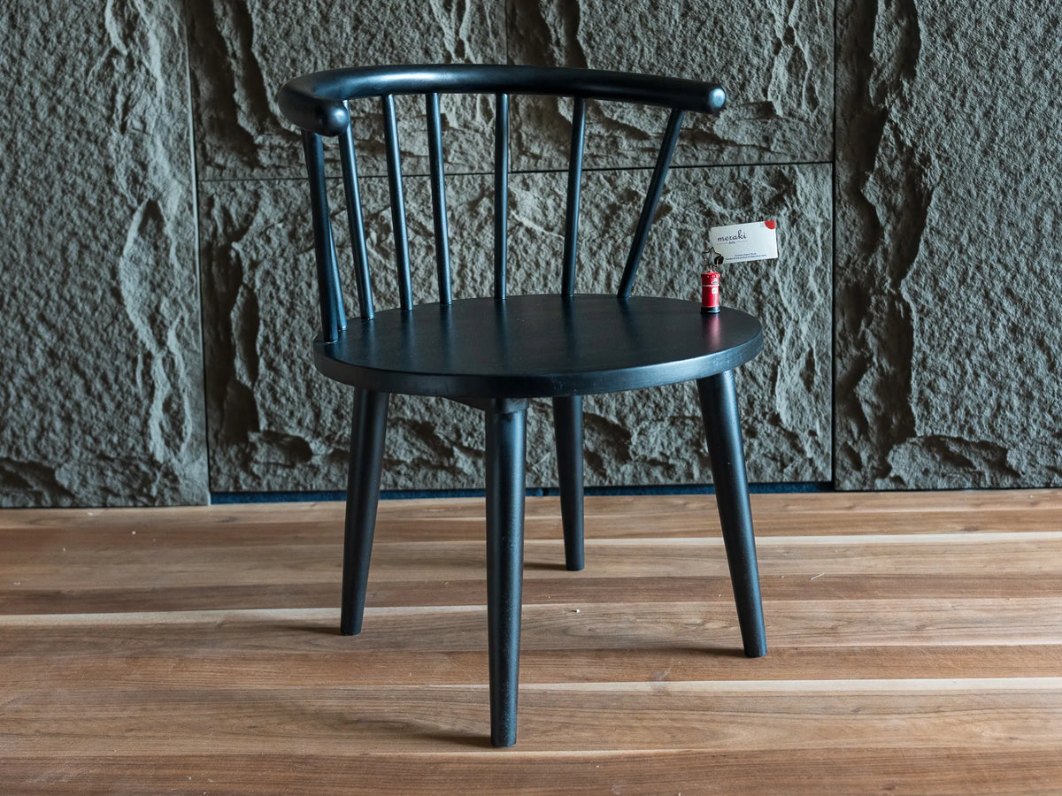 A black wooden dining chair with a curved backrest and spindle design, set against a textured gray stone wall and light brown wooden floor.