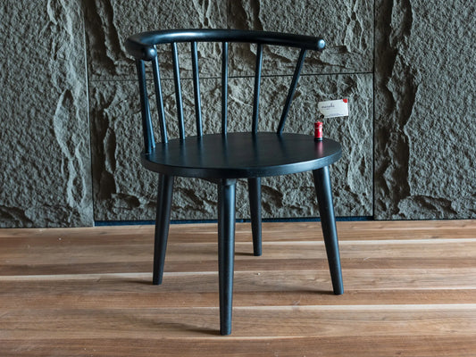 A black wooden dining chair with a curved backrest and spindle design, set against a textured gray stone wall and light brown wooden floor.