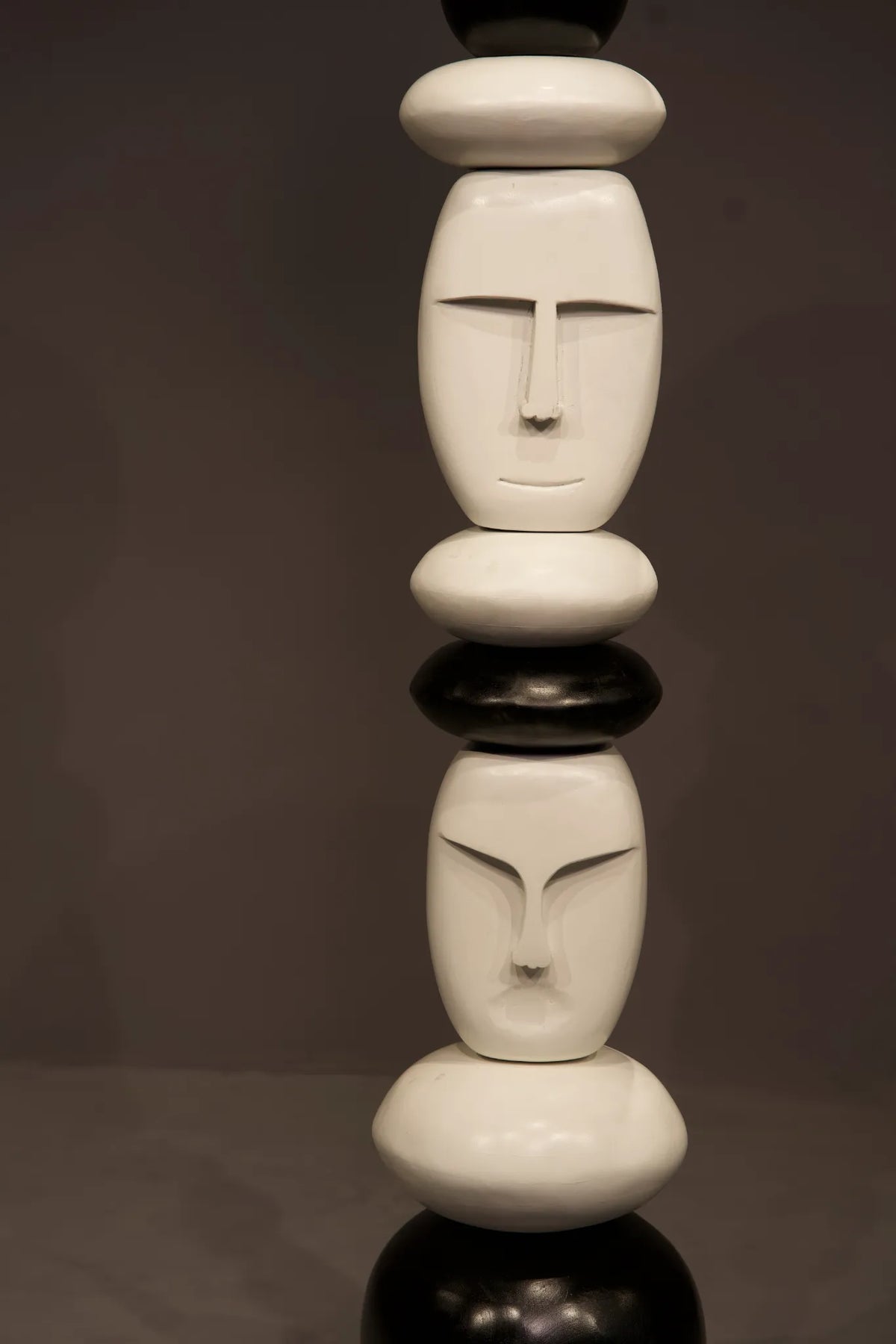 A modern abstract sculpture featuring stacked, rounded organic shapes in glossy white and black, arranged vertically against a dark gray studio background.