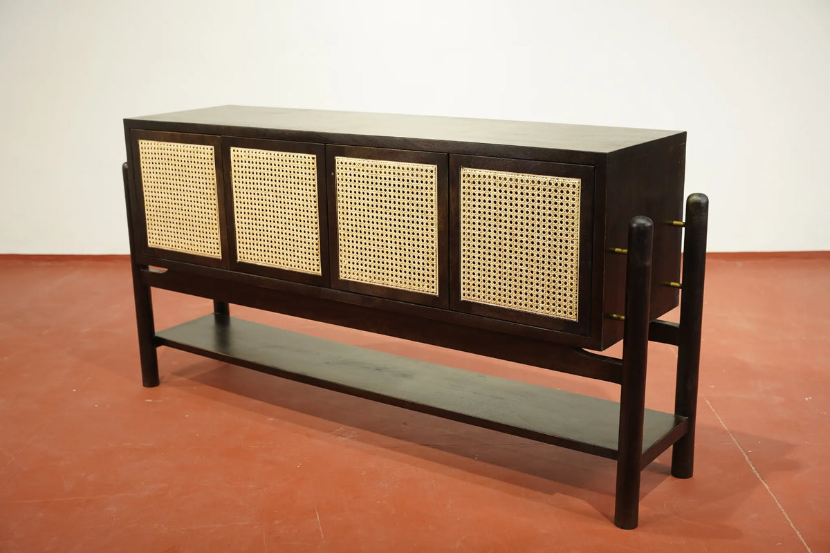 A mid-century modern sideboard cabinet with a dark wood frame, four cane panel doors, and a lower open shelf, set against a plain white wall and terracotta-colored floor.