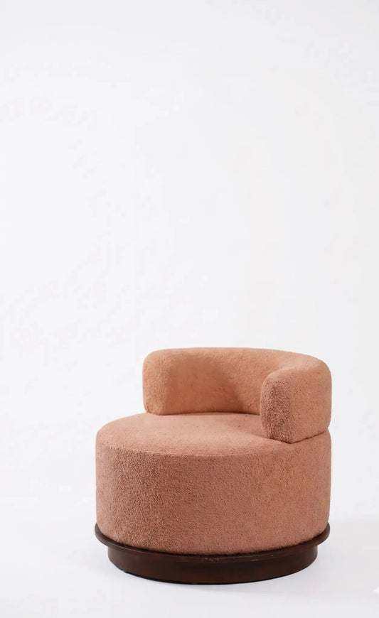 A modern round upholstered accent chair in a dusty rose or terracotta pink fabric, featuring a dark brown wooden base, set against a plain white background.