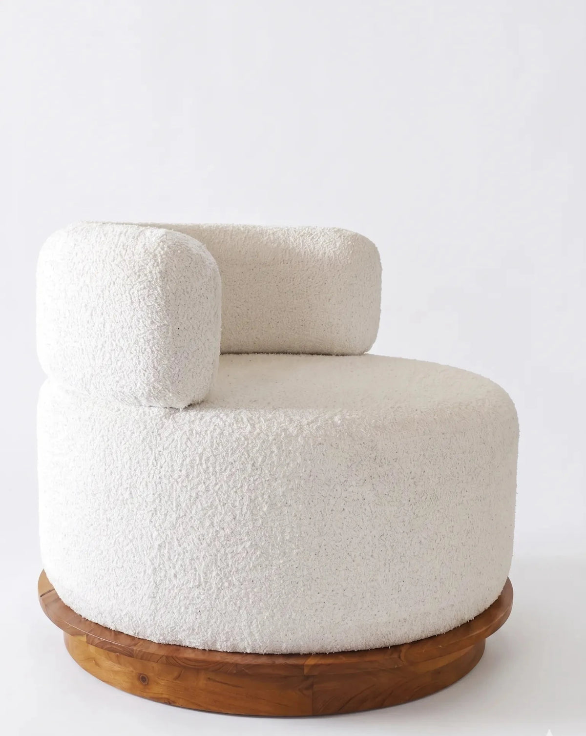 A modern low-profile barrel chair upholstered in textured off-white bouclé fabric, featuring a rounded backrest and a circular natural wood base, photographed against a seamless white background.