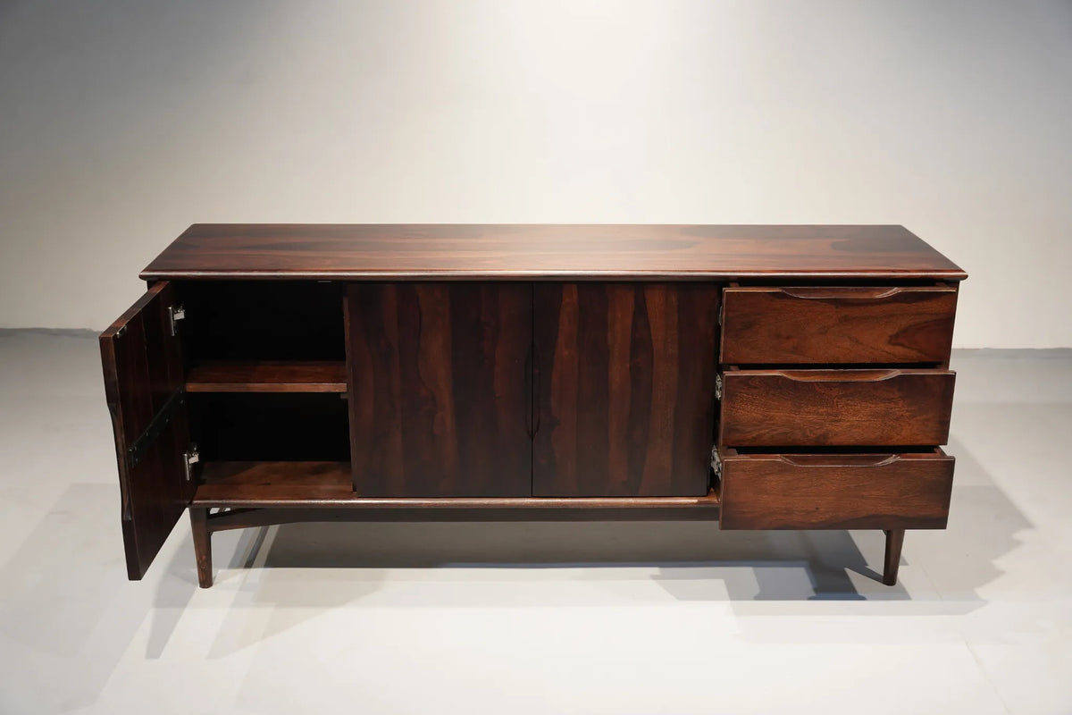 Mid-century modern dark wood sideboard cabinet with an open left cabinet door, two central doors, three drawers on the right, and tapered legs, shown against a plain studio background.