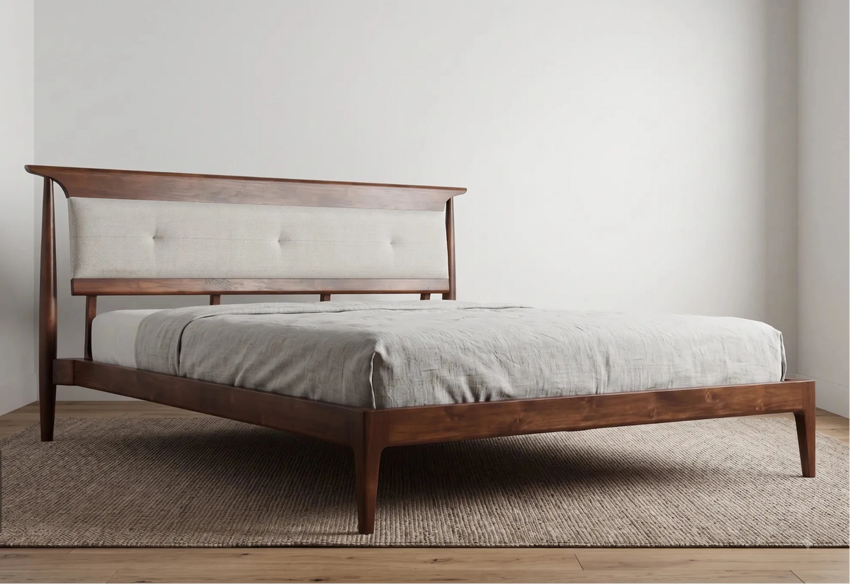 A mid-century modern wooden bed frame with a tufted light beige upholstered headboard, shown with a light gray linen sheet and duvet in a minimalist bedroom setting.